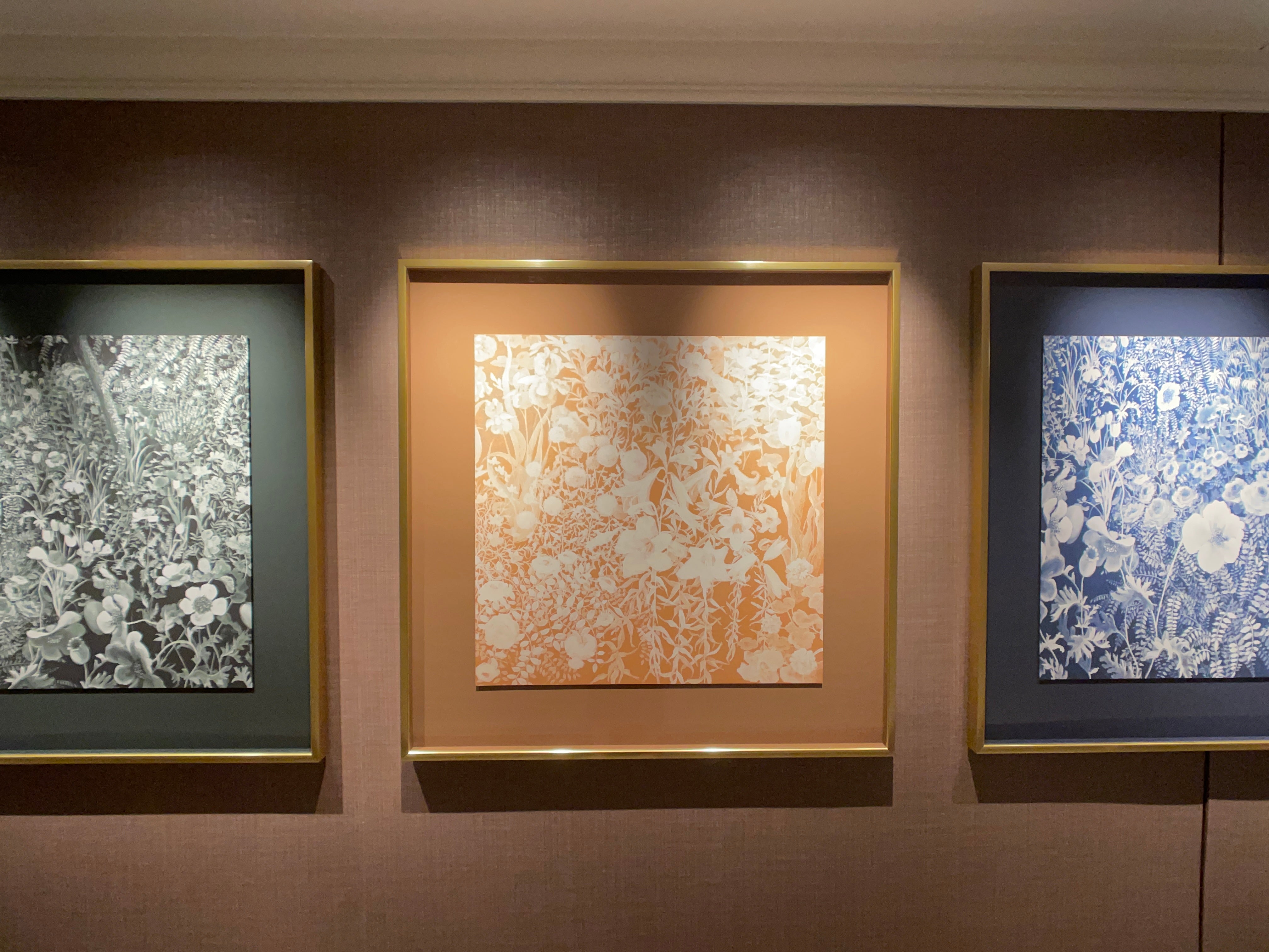 Brassy gold framed prints, one black, one yellow ochre and one navy blue, by Alice Denison hang in a row on the wall.